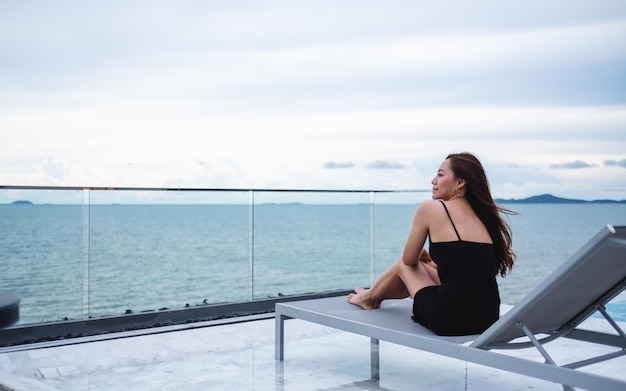 Eine schöne junge Asiatin, die neben dem Pool auf dem Dach sitzt und auf das Meer und den blauen Himmel blickt?