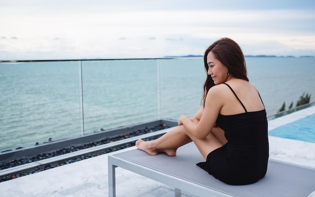 Eine schöne junge Asiatin, die neben dem Pool auf dem Dach sitzt und auf das Meer und den blauen Himmel blickt?