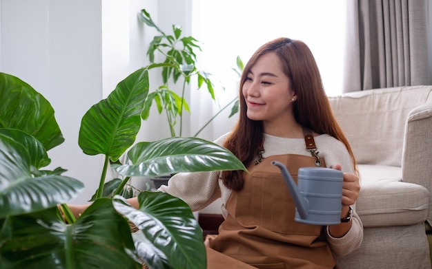 Eine schöne junge Asiatin, die sich zu Hause um Zimmerpflanzen kümmert und sie mit einer Gießkanne gießt