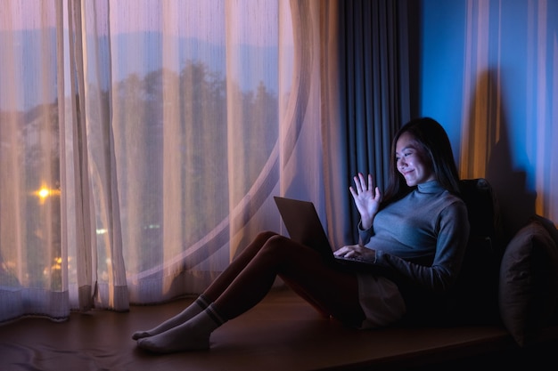 Eine schöne junge asiatin, die spät in der nacht zu hause einen laptop für videoanrufe mit hellem lichtschirm verwendet