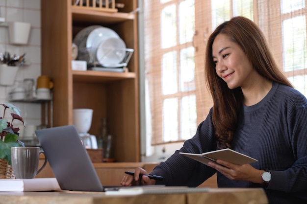 Eine schöne junge asiatische Frau, die einen Laptop-Computer verwendet, um zu Hause online zu arbeiten oder zu lernen