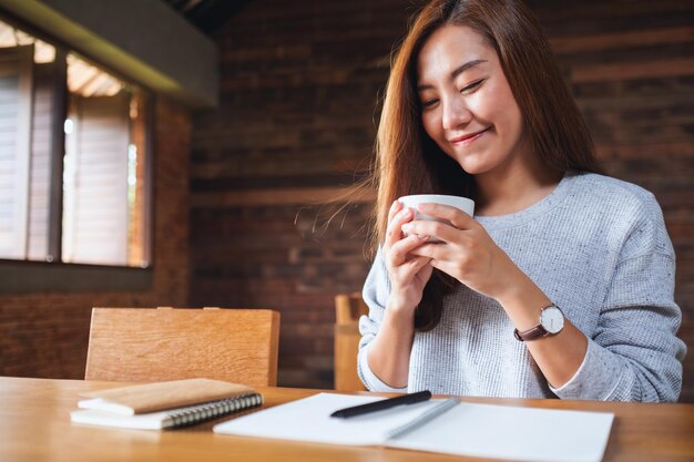 Eine schöne junge asiatische Frau, die Kaffee trinkt, während sie zu Hause arbeitet und studiert