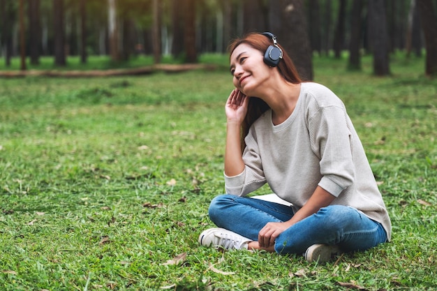 Eine schöne junge asiatische frau hört gerne musik mit kopfhörern und fühlt sich glücklich und entspannt im park