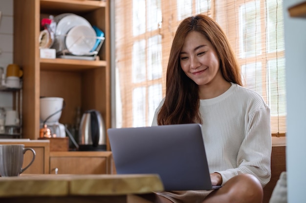 Eine schöne junge asiatische Freiberuflerin, die einen Laptop-Computer verwendet, um zu Hause online zu arbeiten