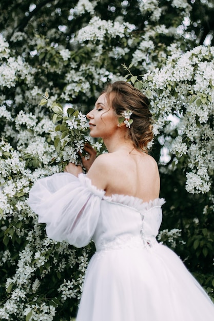 Eine schöne junge Braut in einem Hochzeitskleid geht allein in einem blühenden Frühlingspark im Freien