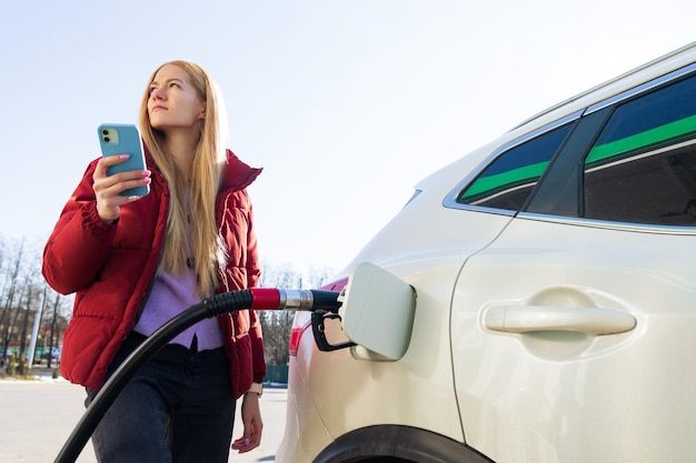 Eine schöne junge Frau bezahlt mit einer App auf ihrem Handy für eine Tankstelle