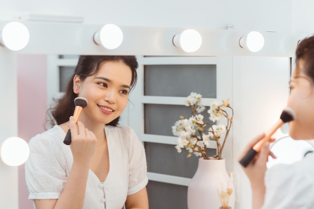 Eine schöne junge Frau, die an einem Make-up-Tisch sitzt und ihr Make-up tut.