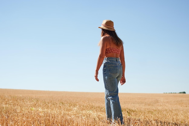 Eine schöne junge Frau, die an einem sonnigen Tag auf dem Land in einem Weizenfeld steht