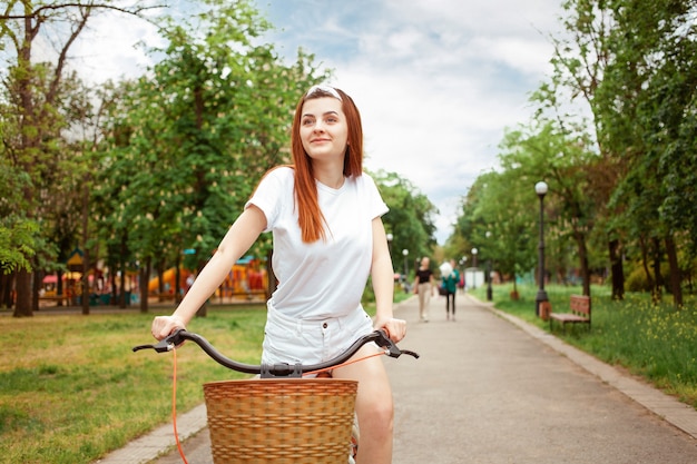 Eine schöne junge Frau fährt mit ihrem Fahrrad im Park. Mieten Sie Transport für den Tag. Sommer Frühling. Das glückliche Mädchen lächelt. Gesunder Lebensstil des Sports, im Freien.