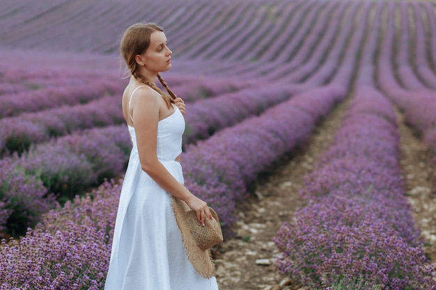 Eine schöne junge frau in einem weißen kleid mit hut geht durch ein lavendelfeld