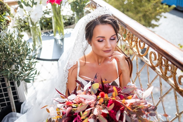 Eine schöne junge Frau in exquisiten Dessous steht auf dem Balkon eines mehrstöckigen Gebäudes und hält einen großen Blumenstrauß in ihren Händen Morgen der Braut am Hochzeitstag
