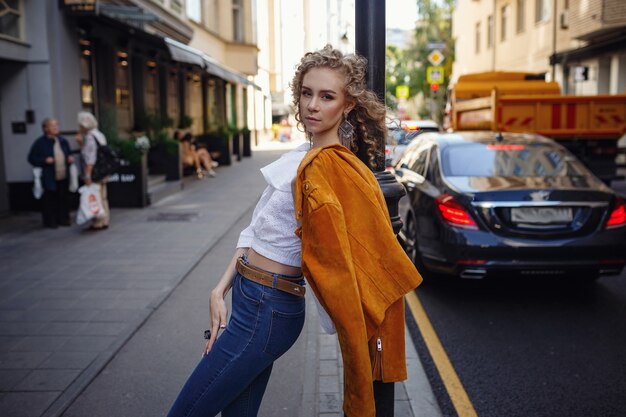 Eine schöne junge Frau mit blonden Locken geht durch die sonnige Stadt und genießt einen Mittagsspaziergang.