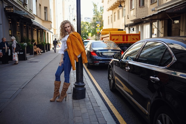 Eine schöne junge Frau mit blonden Locken geht durch die sonnige Stadt und genießt einen Mittagsspaziergang.