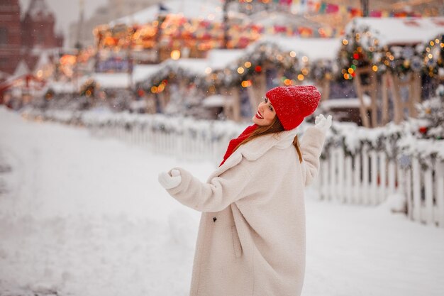 Eine schöne junge Frau mit rotem Hut und warmer Kleidung amüsiert sich auf dem Weihnachtsmarkt in Moskau auf dem Roten Platz