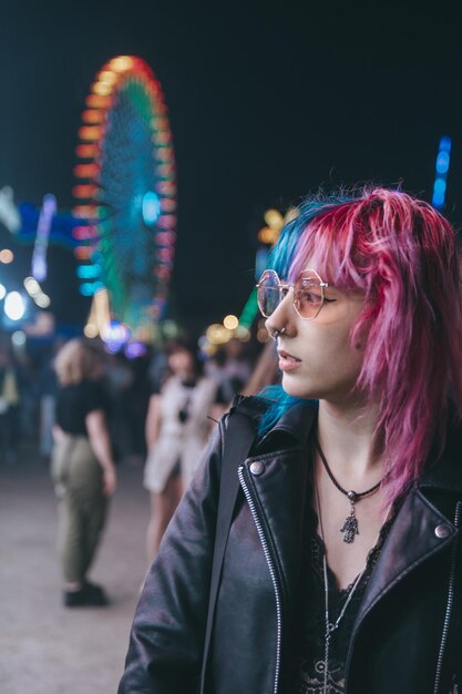 Foto eine schöne junge frau mit sonnenbrille und lederjacke vor einem beleuchteten vergnügungspark bei nacht