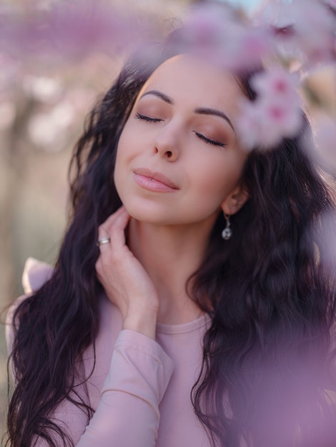 Eine schöne junge Frau nahe einem blühenden Frühlingskirschblütenbaum. Ein Fest des Frühlings und der Blüte wie in Japan