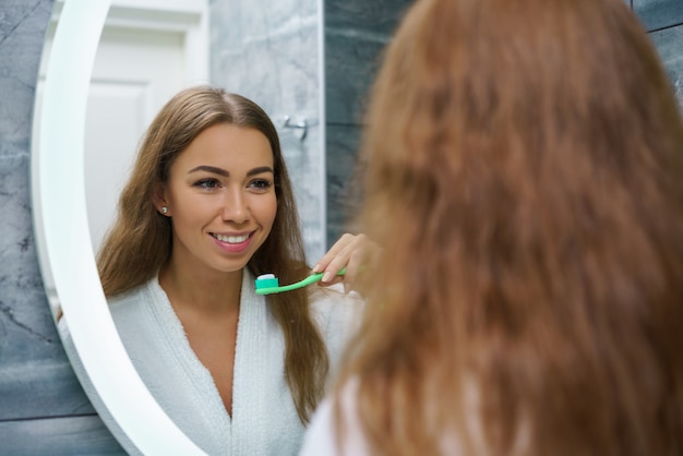 Foto eine schöne junge frau putzt sich die zähne und schaut in den spiegel