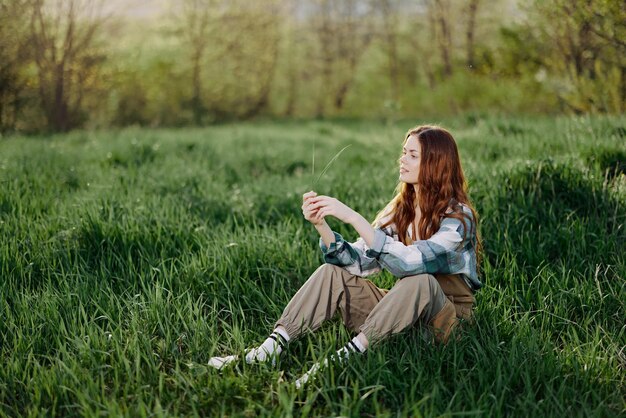 Foto eine schöne junge frau sitzt auf dem grünen gras im park und schaut in die untergehende sonne.