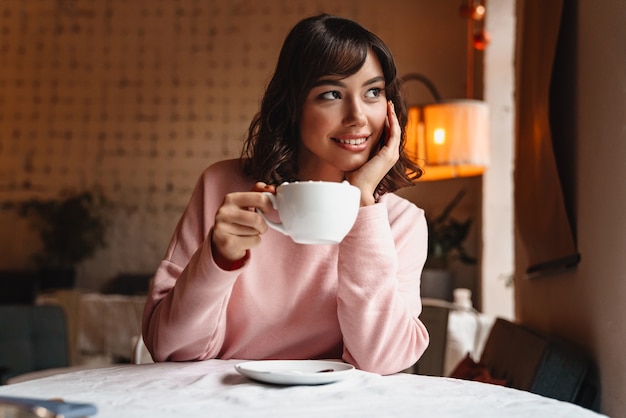 Eine schöne junge hübsche glückliche Frau drinnen im Café, das Kaffee mit Marshmallow trinkt.