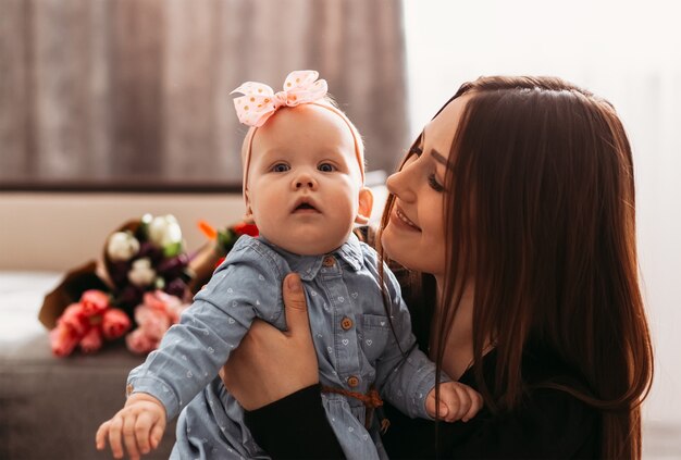 Eine schöne junge Mutter hält ihre Tochter in den Armen und lächelt. Eltern und Kinder