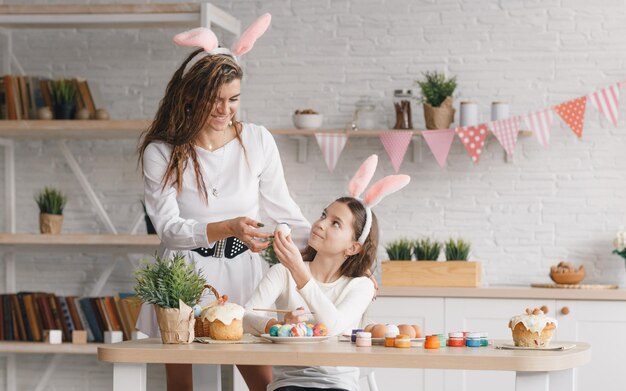 Eine schöne junge Mutter und ihre kleine Tochter bereiten sich gemeinsam auf die Osterferien vor und bemalen Ostereier in der heimischen Küche. Festliche Stimmung