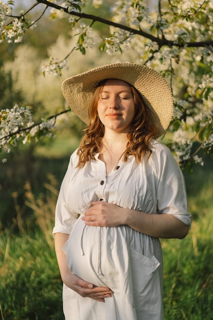 Eine schöne junge schwangere Frau in einem weißen Kleid geht in den Frühlingsgarten