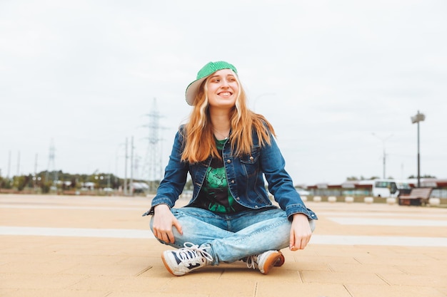 Eine schöne junge Teenagerin in Mütze und Jeansjacke sitzt über einer Skateboard-Generation z