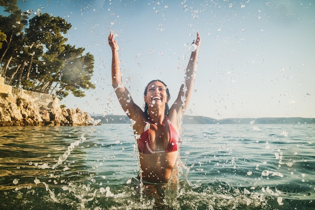 Eine schöne lächelnde Frau, die Spaß hat und im Meerwasser spritzt. Sie genießt im Urlaub.