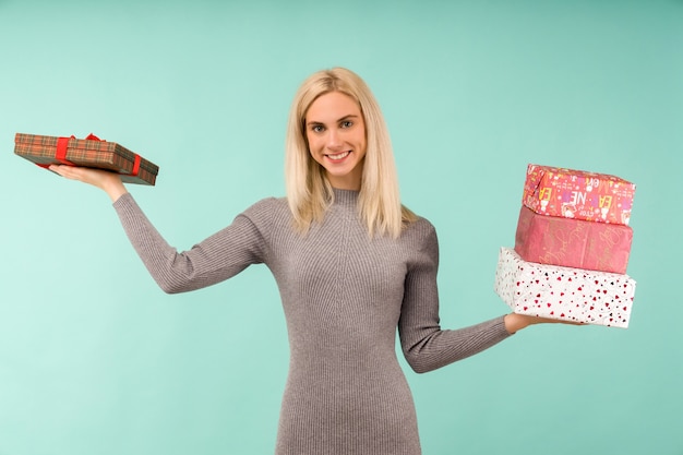 Eine schöne lächelnde Frau in einem grauen Kleid, in den Händen Geschenke halten. Feier von Weihnachten oder Neujahr auf blauem Hintergrund