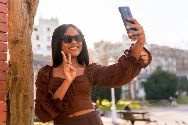 Eine schöne natürliche junge Afrikanerin in einem Park mit Sonnenbrille, die bei Sonnenuntergang ein Selfie macht