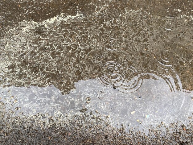 Eine schöne Oberfläche aus blühendem Regenwasser mit gelben und weißen Streifen und Kreisen in einer Pfütze