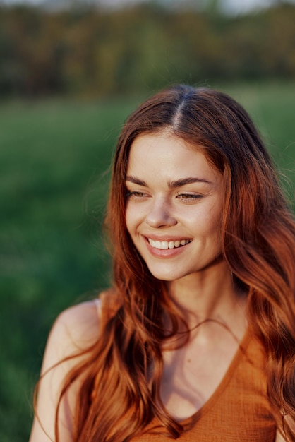 Eine schöne rothaarige Frau lacht und lächelt mit ihren Zähnen im hellen Sonnenlicht des Sonnenuntergangs. Das Konzept eines gesunden Lebens und einer guten Ernährung