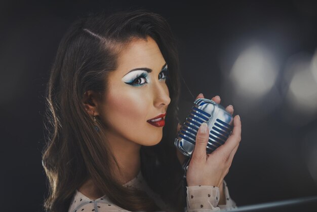 Eine schöne Sängerin mit stylischem Retro-Haar und Make-up hält ein Vintage-Mikrofon mit Ständer bereit zum Singen.