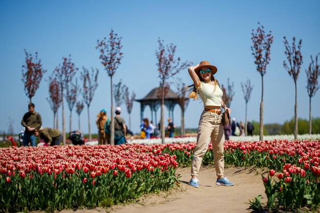 Eine schöne schlanke Frau mit Hut steht in einem blühenden Tulpenfeld. Frühlingszeit