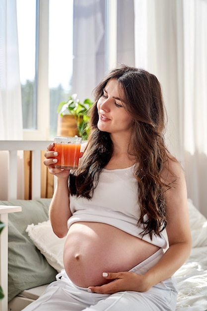 Eine schöne schwangere Frau isst richtig und trinkt frischen Natursaft