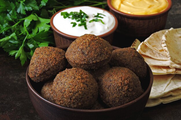 Foto eine schüssel falafel, weiße sauce, pita und petersilie. frische falafel.