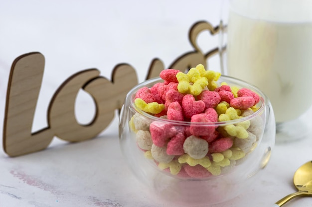 Eine Schüssel Frühstücksflocken, ein Glas Milch und eine hölzerne Liebesinschrift auf einem weißen Tisch Romantisches Frühstück