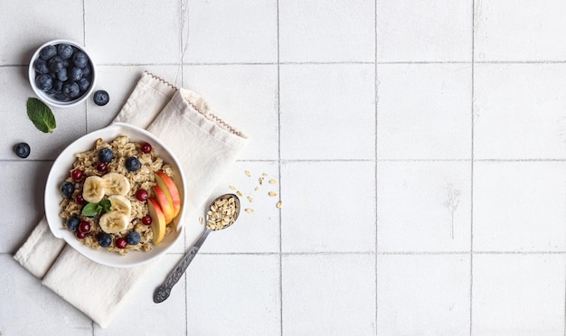 Eine Schüssel Haferflocken mit Obst und Müsli auf einem weißen Fliesenhintergrund.