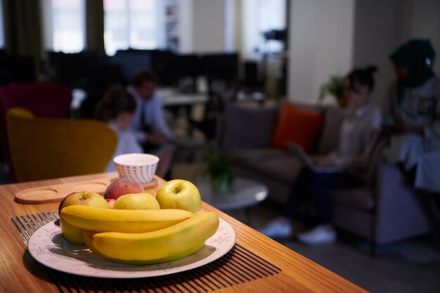 Eine Schüssel mit frischen Früchten im Entspannungsbereich mit Geschäftsleuten im Hintergrund im modernen Startup-Büro