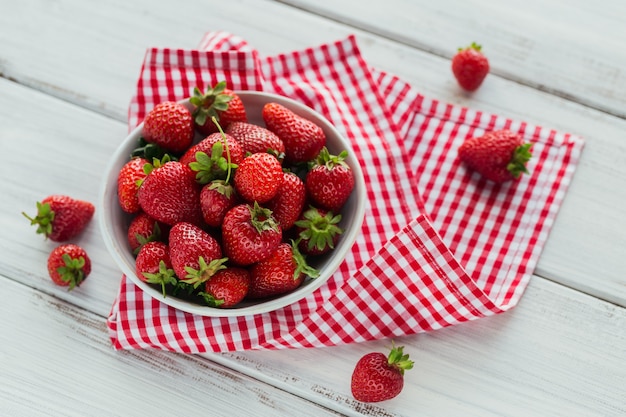 Eine Schüssel mit roten saftigen Erdbeeren auf weißem Holztisch