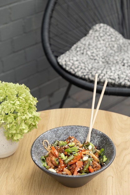 Eine Schüssel mit Udon-Nudeln, Kalbfleisch und gebratenem Gemüse auf einem Holztisch