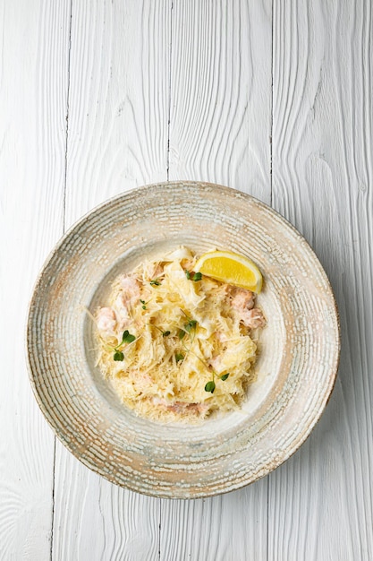 Eine Schüssel Nudeln mit Lachs und Zitrone auf einem weißen Holztisch