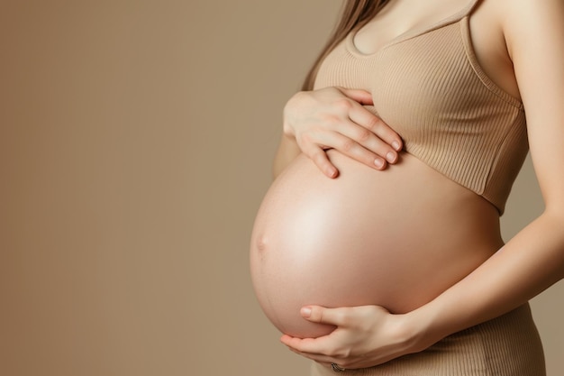 Eine schwangere Frau im neunten Monat berührt ihren Bauch gegen einen beigen Hintergrund mit Kopierraum