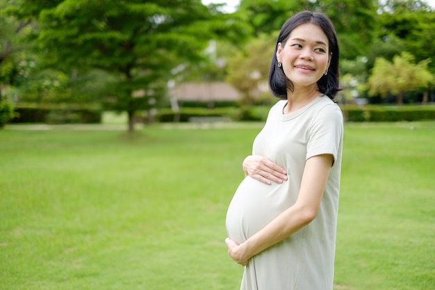 Eine schwangere Frau in einem langen Kleid posiert glücklich lächelnd im Garten.