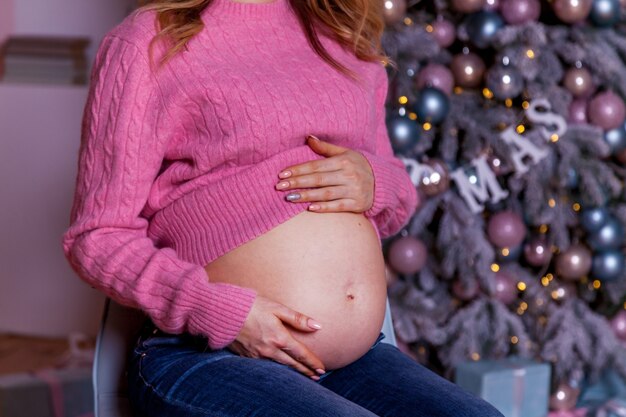 Eine schwangere Frau in einem rosa Pullover sitzt vor einem Weihnachtshintergrund