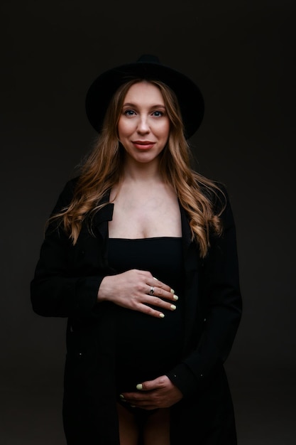 Eine schwangere Frau in schwarzem Anzug und schwarzem Hut. Platz zum Kopieren. Das Konzept der gesunden Verdauung, des Lebensstils, IVF
