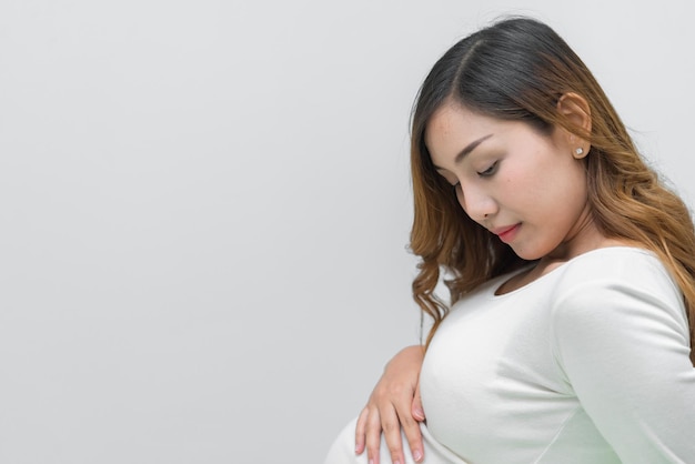 Eine schwangere Frau in weißem Kleid steht für ein Foto auf weißem Hintergrund