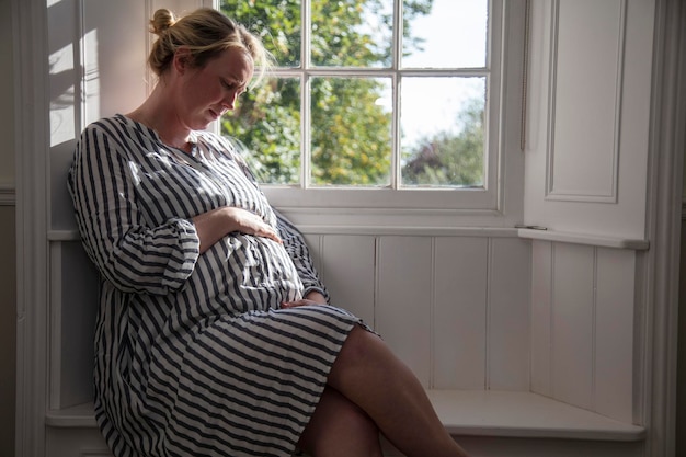 Eine schwangere Frau sitzt am Fenster