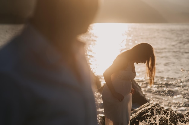 Eine schwangere Frau steht auf einem Felsen vor einem Sonnenuntergang.