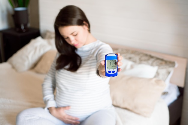 Eine schwangere Frau überprüft ihren Blutzucker mit einem Blutzuckermessgerät. Schwangerschaftsdiabetes